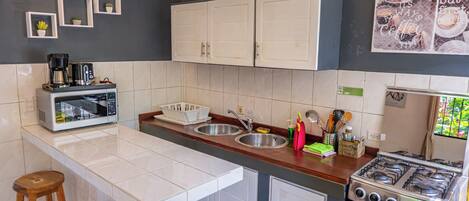 A compact kitchen with white cabinets, a gas stove, a coffee maker, and a sink.