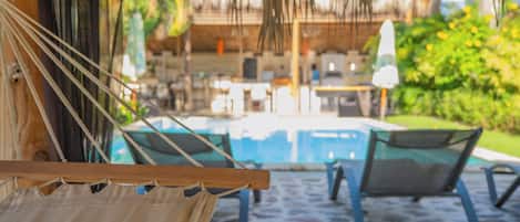 A hammock, a pool, and lounge chairs in a tropical setting.