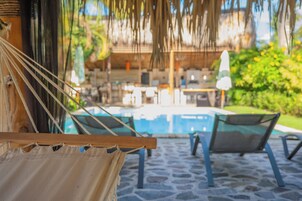 Una hamaca, una piscina y sillas de descanso en un entorno tropical.