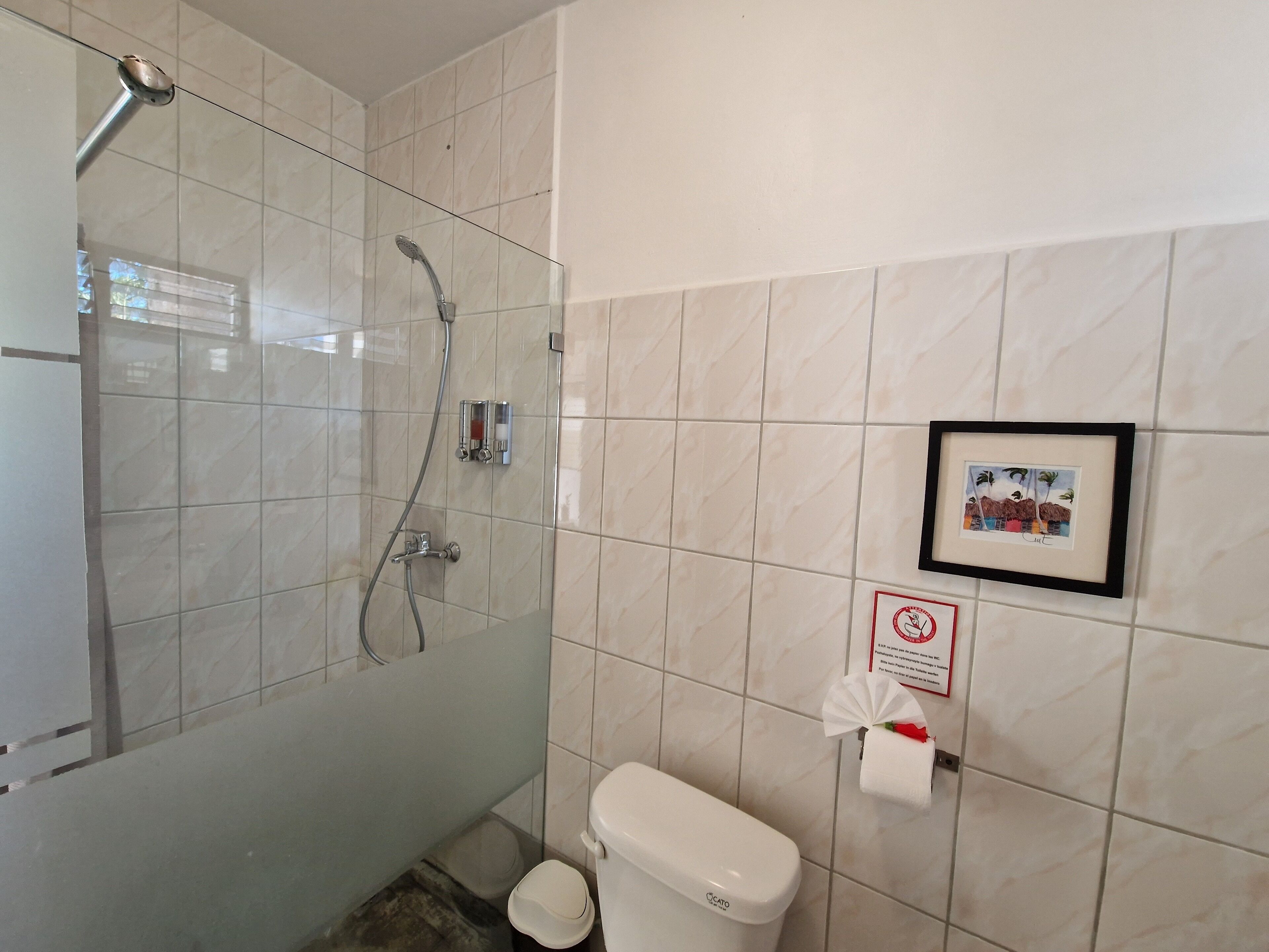 Ein Badezimmer mit einer gläsernen Duschkabine, einer Toilette und einem gerahmten Bild an der Wand.