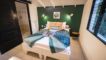 A bedroom with a bed, a small bedside table, a wall-mounted light, and a window with a metal grill.