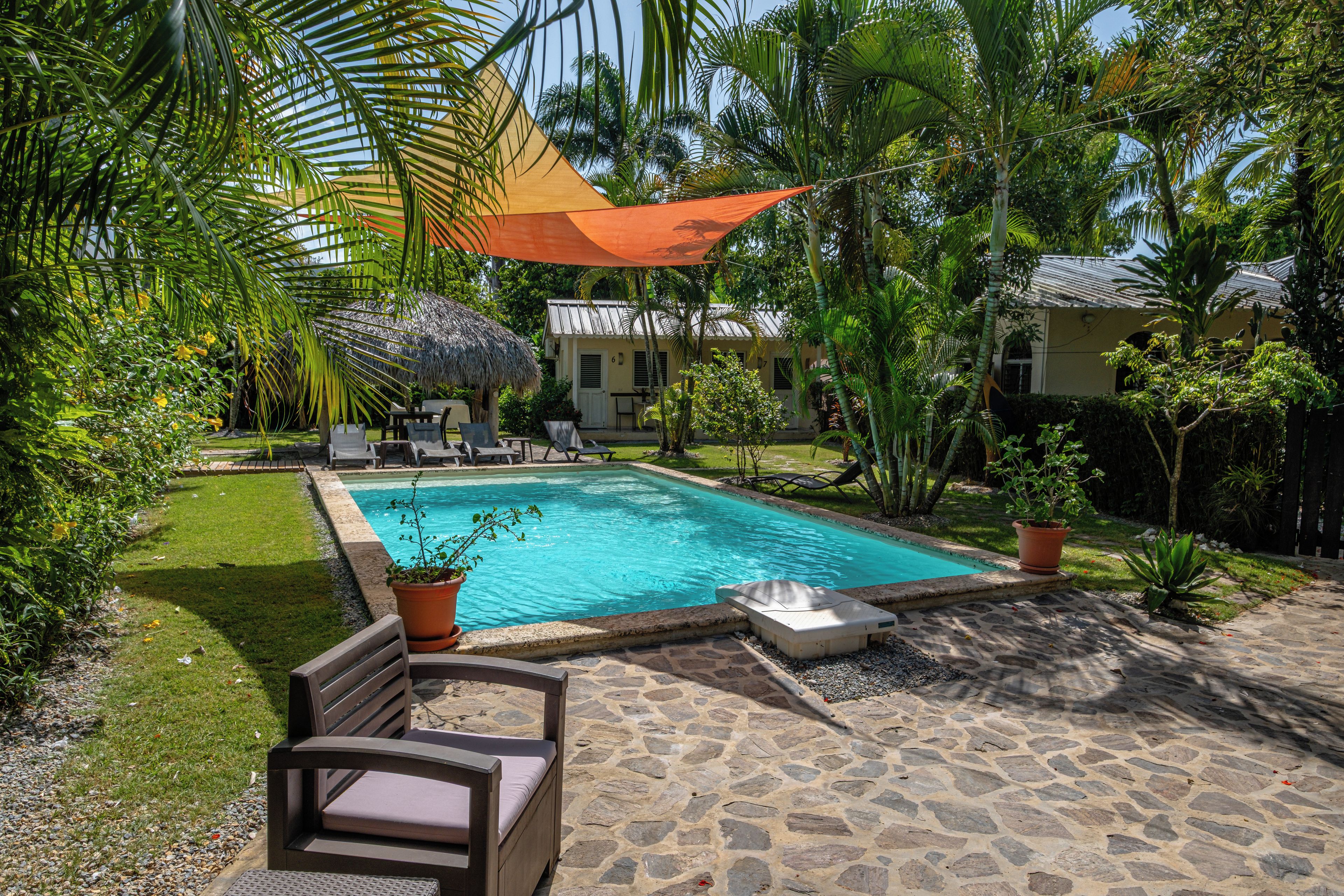 Un área de piscina con un patio de piedra, sillas de descanso y una estructura de techo de paja.