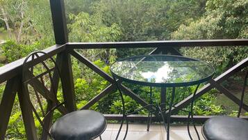 Een balkon met een glazen tafel en twee zwarte stoelen, omringd door weelderige begroeiing.