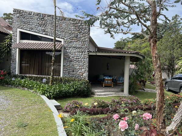 A modern house with a stone facade, a covered porch, and a garden with various plants and flowers. - Hotel Dos Rios (Nueva California)