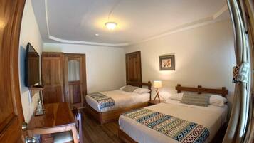 A hotel room with two single beds, a wooden desk, a chair, a television, and a ceiling light.