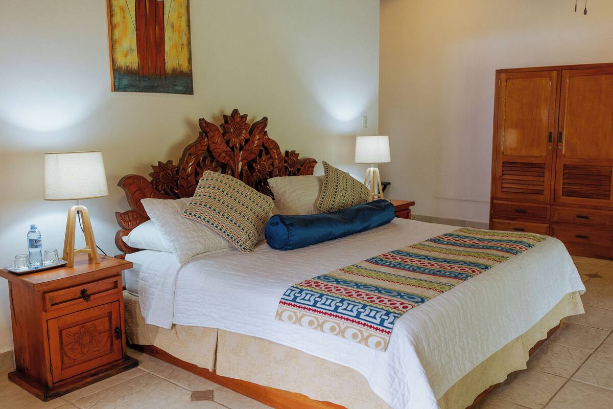 A neatly made bed with a patterned bedspread, a wooden headboard, and a nightstand with a lamp and a bottle.