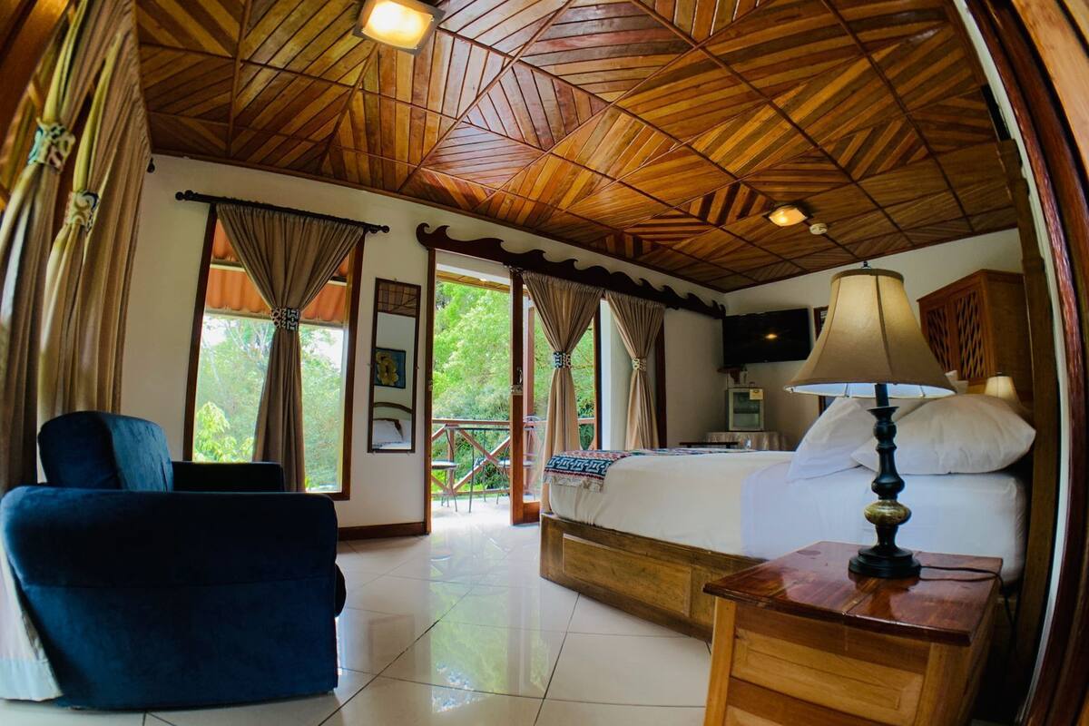 A room with a wooden ceiling, a bed, a desk, a chair, and a TV.