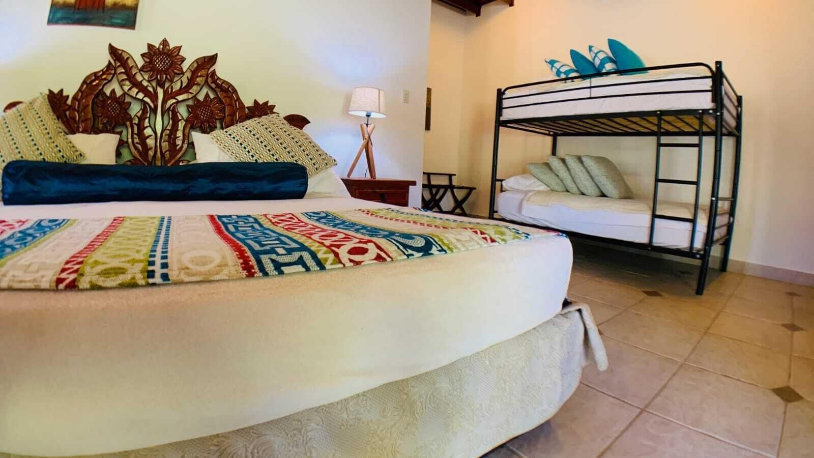 Un dormitorio con una cama grande, una cama litera, un cabecero decorativo, una lámpara y una pequeña mesa.
