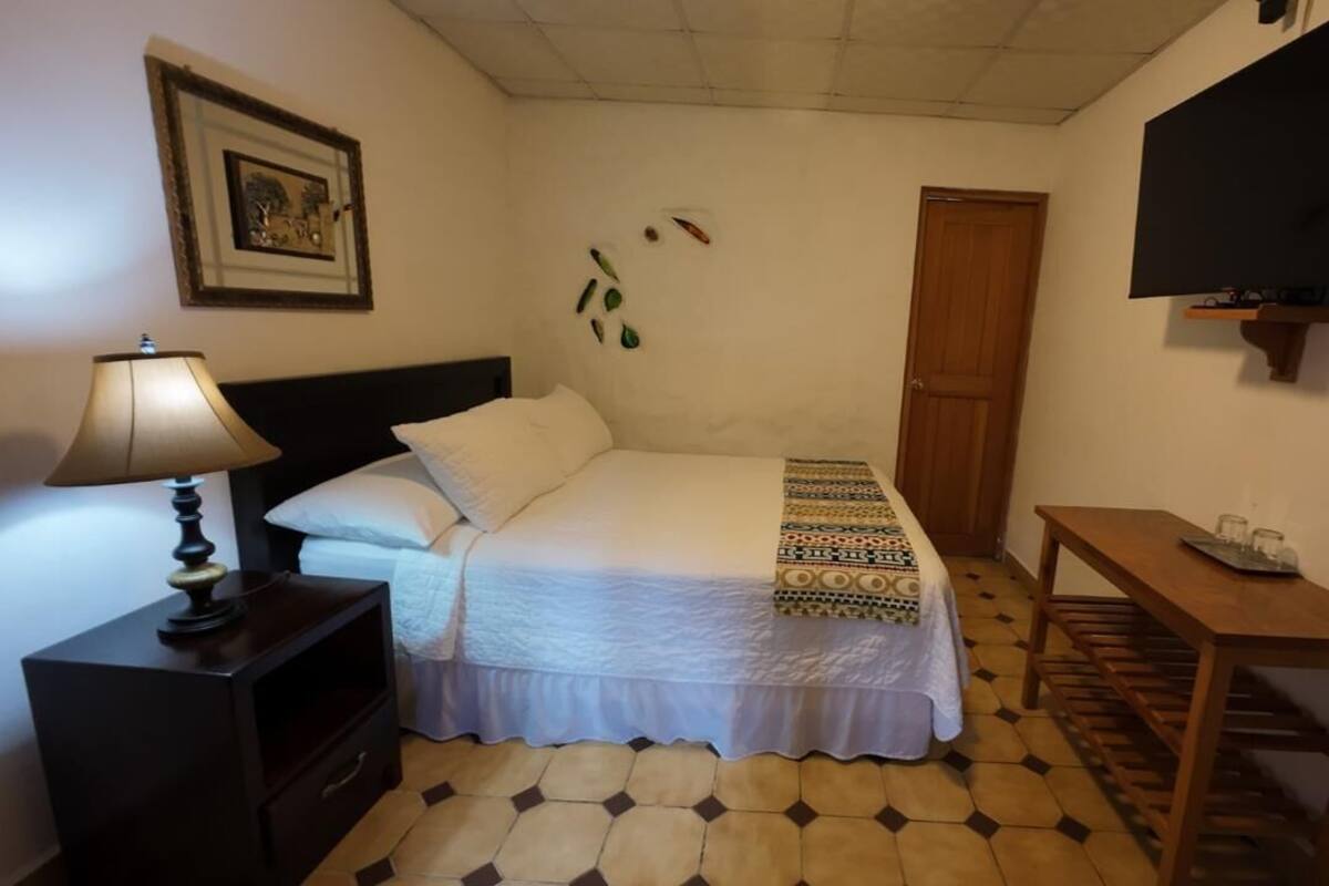 A bedroom with a bed, a nightstand, a table, a TV, and a door.