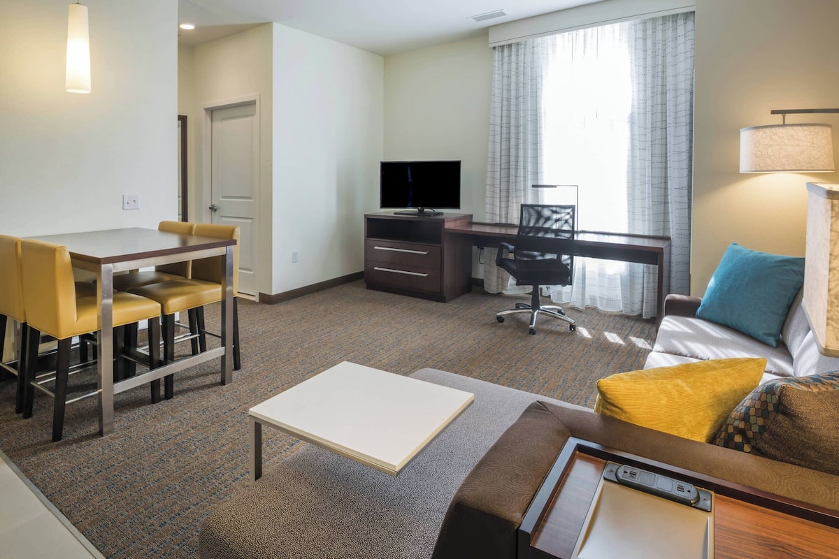 A hotel room with a dining table, a TV, a desk, a couch, and a lamp.