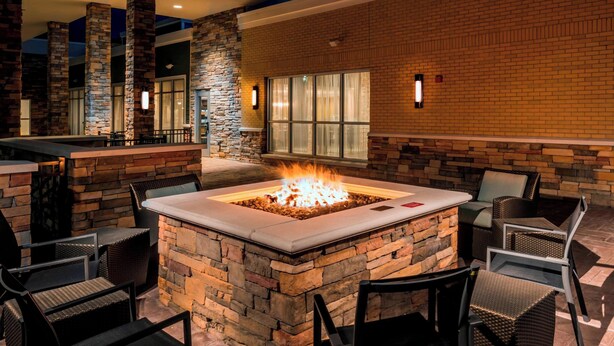 An outdoor patio with a stone fire pit surrounded by wicker chairs and a table. - Residence Inn by Marriott Fishkill (Fishkill)