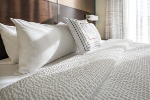 A neatly made bed with white linens and a textured blanket, a wooden headboard, and a bedside table with a lamp.