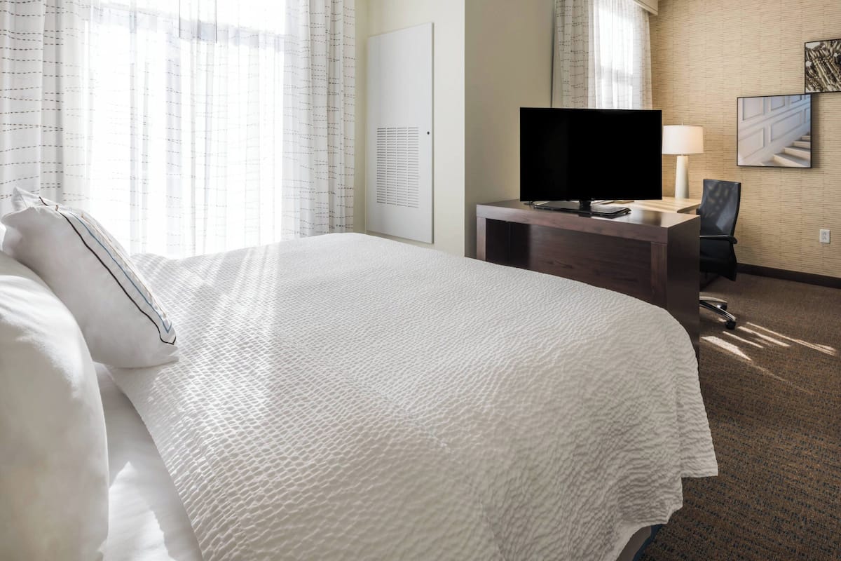 A hotel room with a large bed, a flat-screen TV, a desk with a lamp, and a chair.