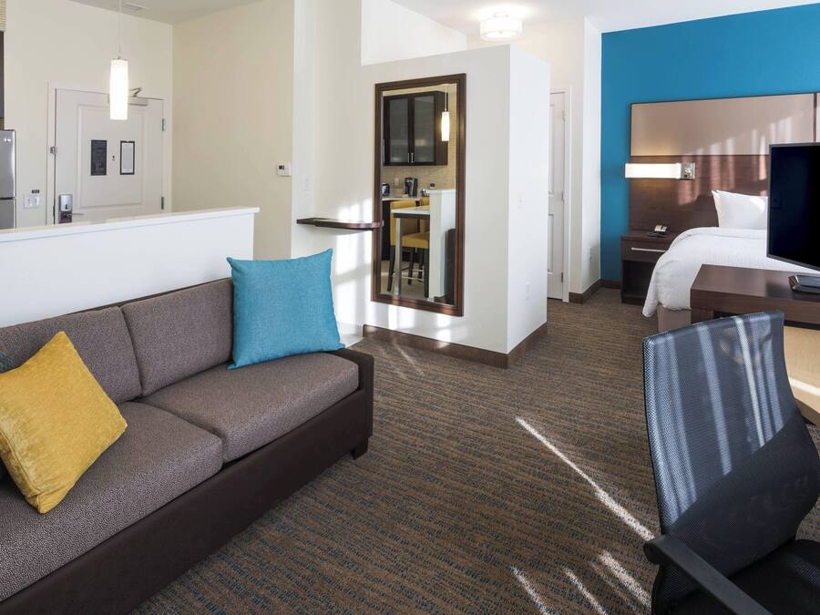 Habitación de hotel con sofá, sillón, cama, televisión, escritorio y zona de cocina.