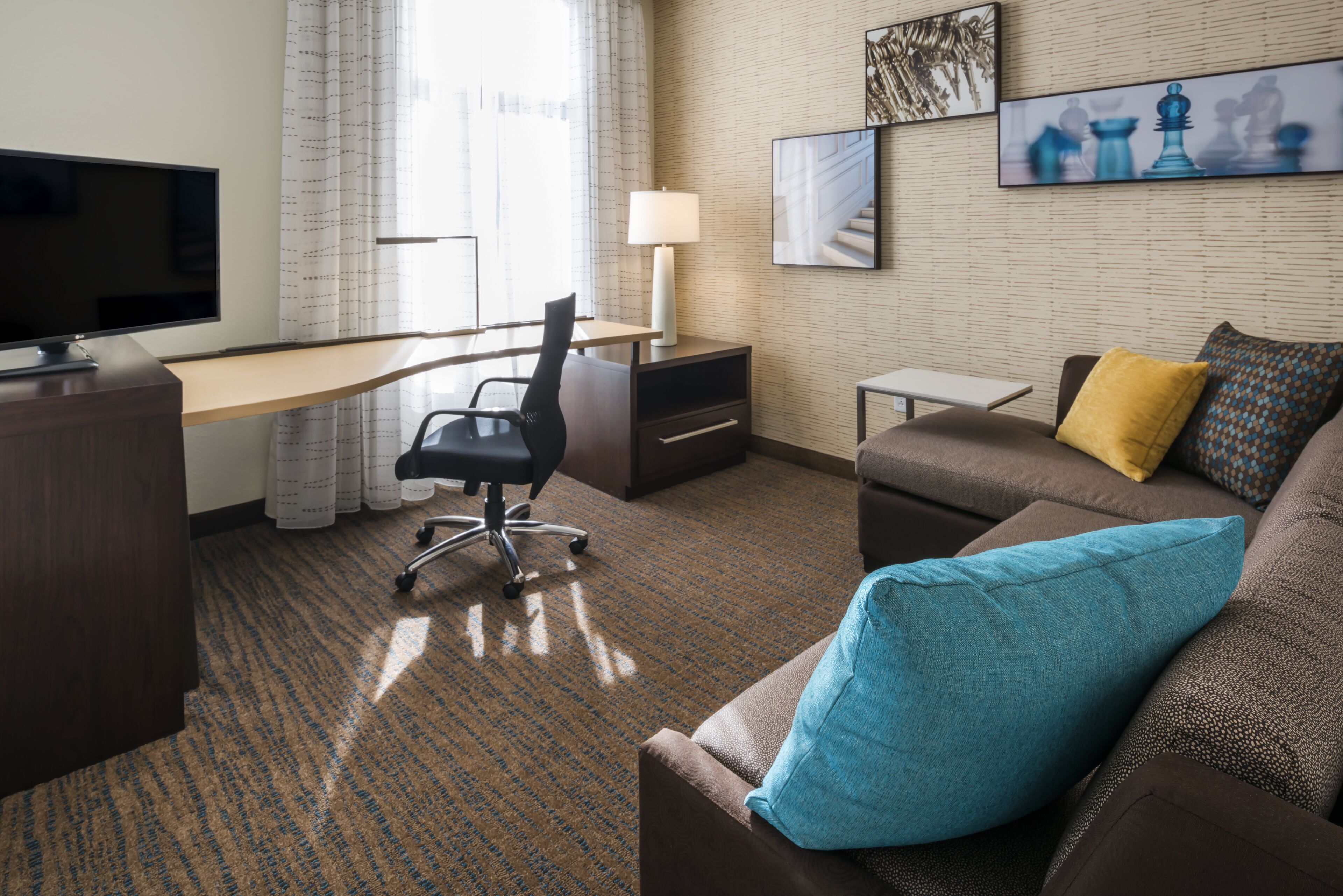 A hotel room with a desk, chair, and a sofa with cushions.