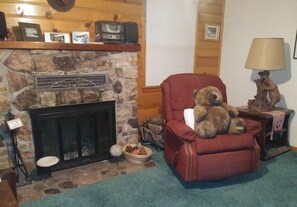 Una sala de estar acogedora con una chimenea de piedra, un sillón rojo, una lámpara y un oso de peluche.