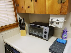 Una cocina con horno tostador, un juego de cuchillos, una botella de lavavajillas y una toalla.