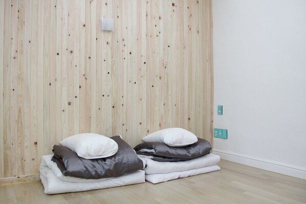 A room with a wooden slat wall, a bed with white and gray bedding, and a teal-colored light switch on the wall.