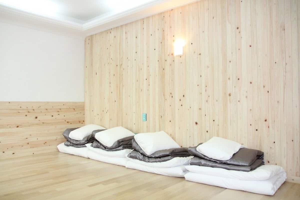 Una habitación con paredes de paneles de madera y suelo de madera. Hay tres camas con ropa de cama blanca y gris.