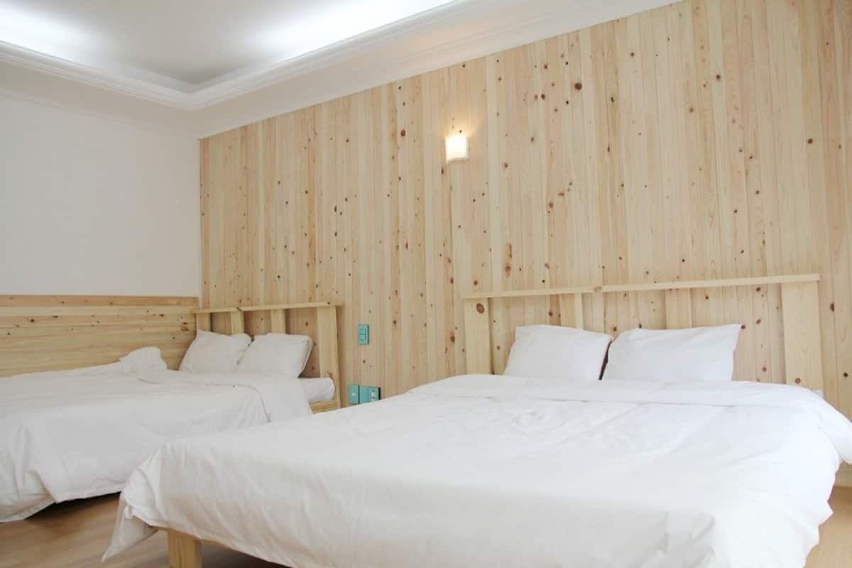 Habitación de hotel con dos camas individuales, paredes de paneles de madera y una lámpara pequeña fijada a la pared.
