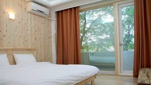 Ein Schlafzimmer mit Holz-Kopfteil, einem Bett mit weißer Bettwäsche und Blick durch eine Schiebetür auf einen Außenbereich.
