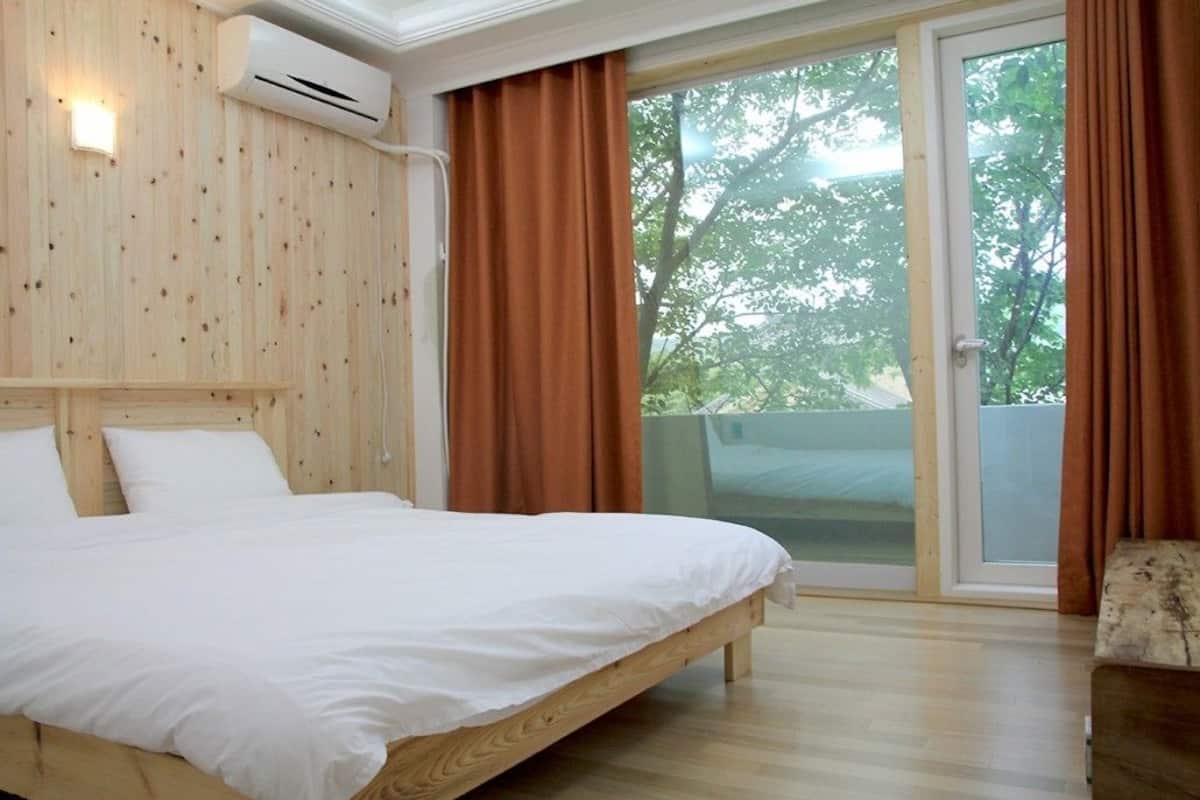 Un dormitorio con cabecera de madera, cama con ropa de cama blanca y vistas a un espacio exterior a través de una puerta corrediza de vidrio.