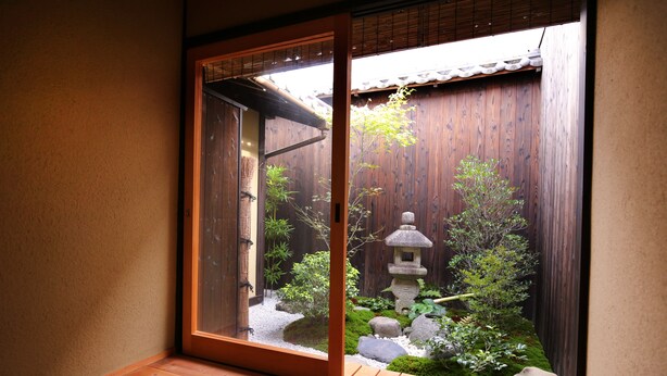 A traditional Japanese garden with a stone lantern, bamboo, and a wooden fence. - Machiya AND (Kyoto)