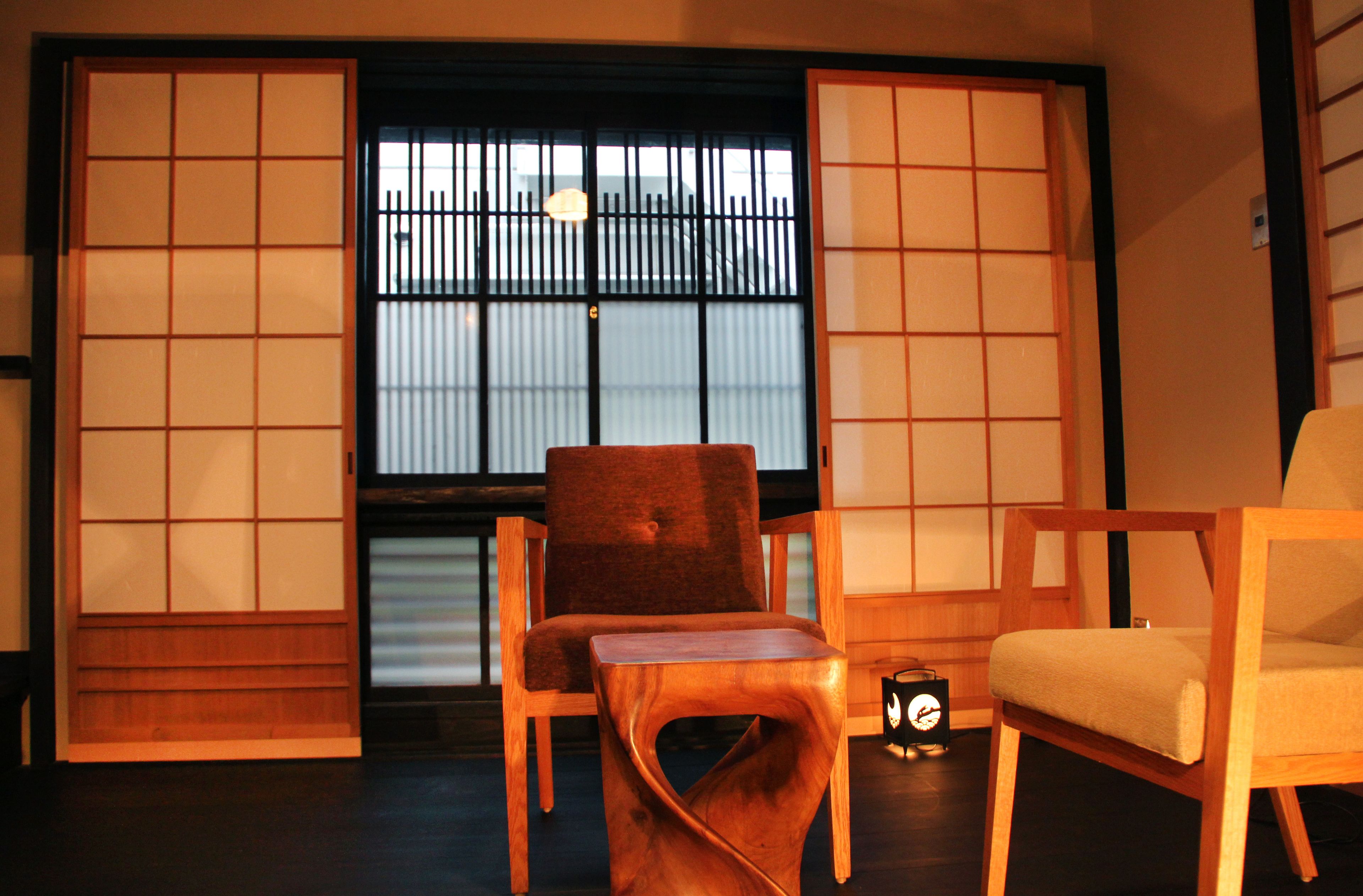 Une pièce de style japonais traditionnel, avec un sol recouvert de tatamis, une porte coulissante en bois et deux chaises.