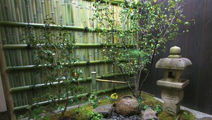 Un jardín japonés tradicional con una valla de bambú, un farol de piedra y diversas plantas.