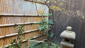 Una valla de bambú, un farol de piedra y un pequeño árbol con flores amarillas.