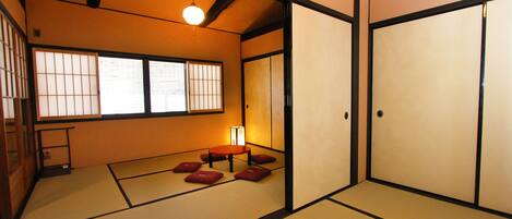 Una habitación japonesa tradicional con suelo de tatami, puertas correderas y una mesa baja con cojines.
