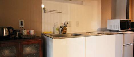 Uma cozinha compacta com pia, micro-ondas e chaleira.