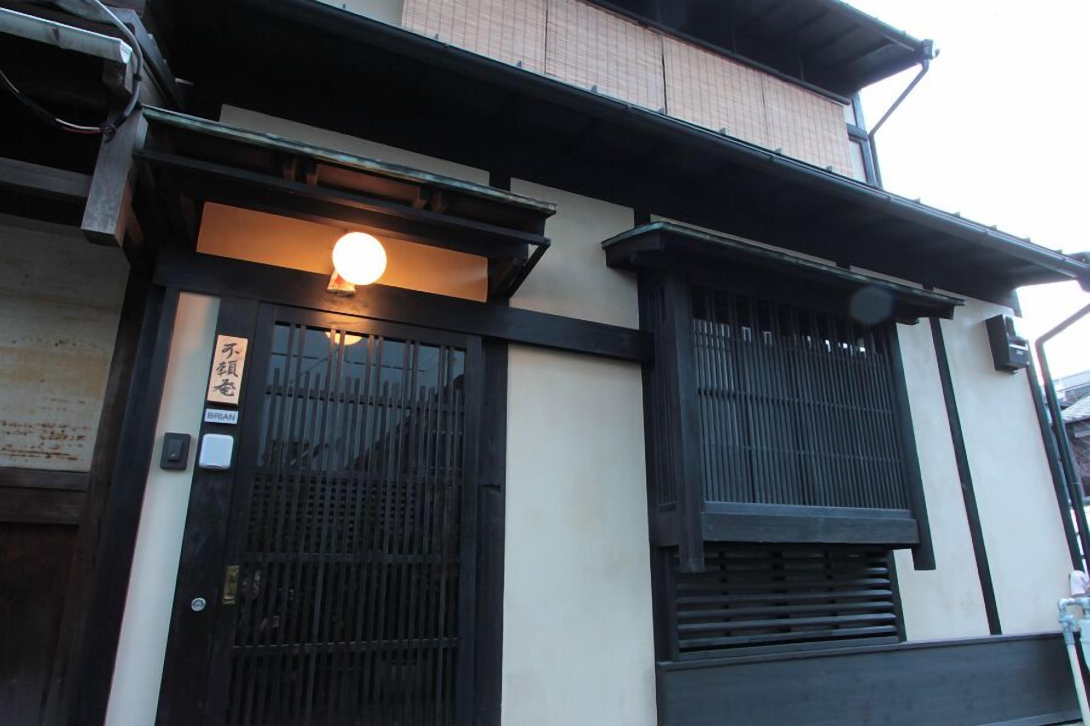 Un bâtiment traditionnel avec un portail noir, une enseigne lumineuse au-dessus de l’entrée et une structure en bois à l’étage supérieur.
