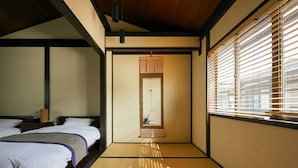 A traditional Japanese-style room with tatami flooring, two beds with white bedding, a shoji screen, and a view through the window blinds. - Kikyo-an (Kyoto)