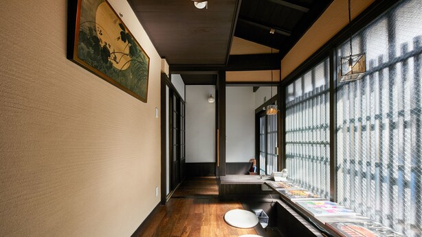 A narrow hallway with wooden flooring, a large window with frosted glass, and a display of colorful items on the right. - Kikyo-an (Kyoto)