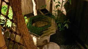 A stone birdbath with moss, surrounded by wooden fencing and greenery. - Kikyo-an (Kyoto)