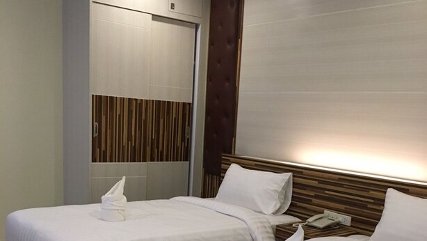 A hotel room with two beds, each with white linens and a towel. There is a wooden headboard, a wall-mounted air conditioning unit, and a wooden panel design on the wall. - Chansuda Lake View Hotel (Ubon Ratchathani)
