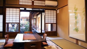 Una habitación japonesa tradicional con suelo de tatami, una mesita baja y puertas correderas que dan a un jardín exterior.