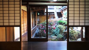 Una habitación tradicional japonesa con suelo de tatami, puertas correderas y vistas a un jardín de rocas y plantas.