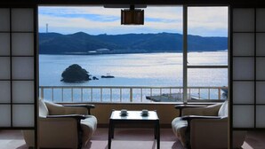 A room with a view of a lake and mountains, featuring a sofa, a small table, and a traditional Japanese sliding door. - Kurofune Hotel (Shimoda)
