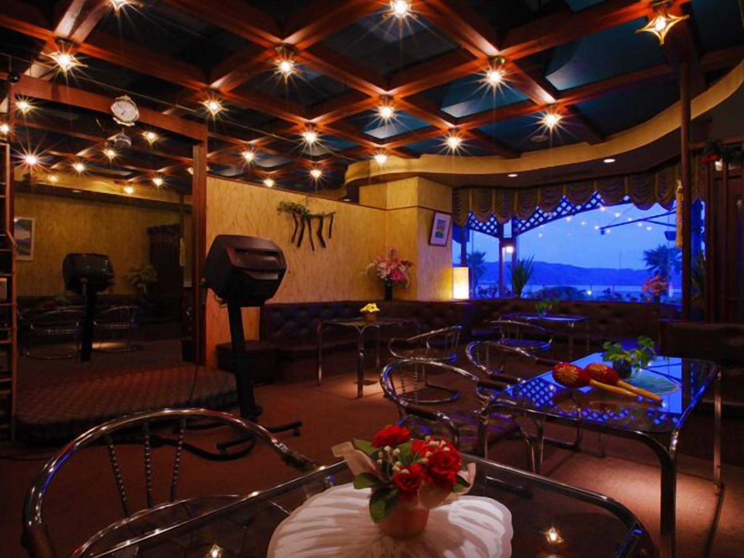A restaurant with a cozy interior, featuring wooden beams, string lights, and a view of the outdoors.