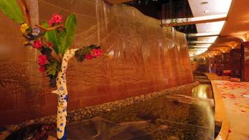 Un espace de détente avec un mur en pierre, un élément décoratif à base d’eau et un vase orné de fleurs.