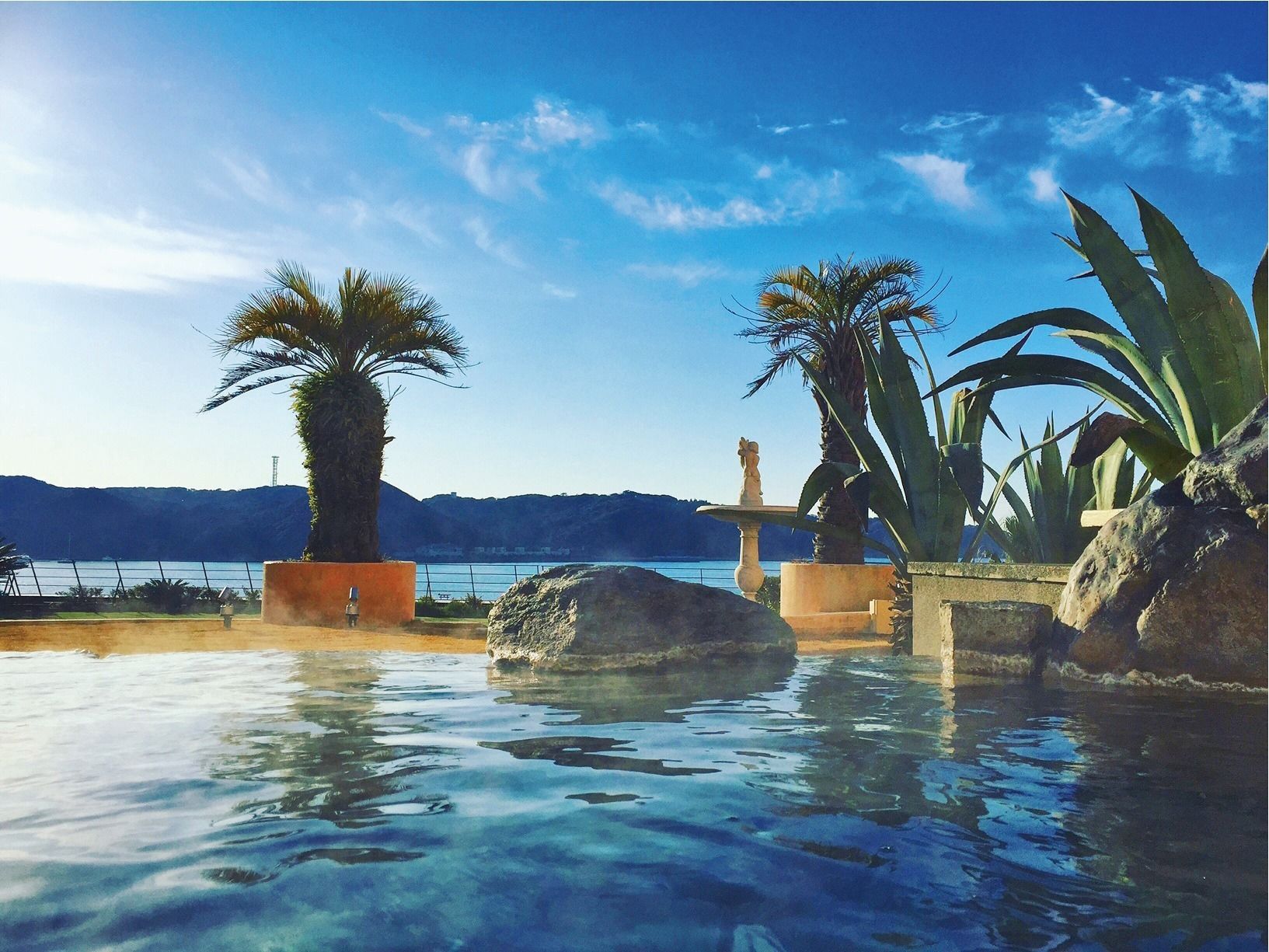 Un área de piscina al aire libre tranquila, con vista despejada a un lago y montañas al fondo.