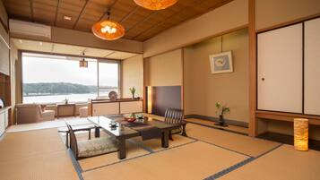 Ein traditioneller japanischer Raum mit Tatami-Böden, einem niedrigen Tisch mit Tee-Set, einem gepolsterten Stuhl und Blick auf ein Gewässer.