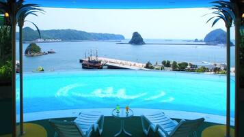 A poolside view with a ship passing by, lounge chairs, and a clear view of the sea and islands.