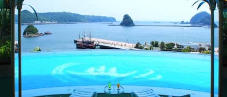 A poolside view with a ship passing by, lounge chairs, and a clear view of the sea and islands.