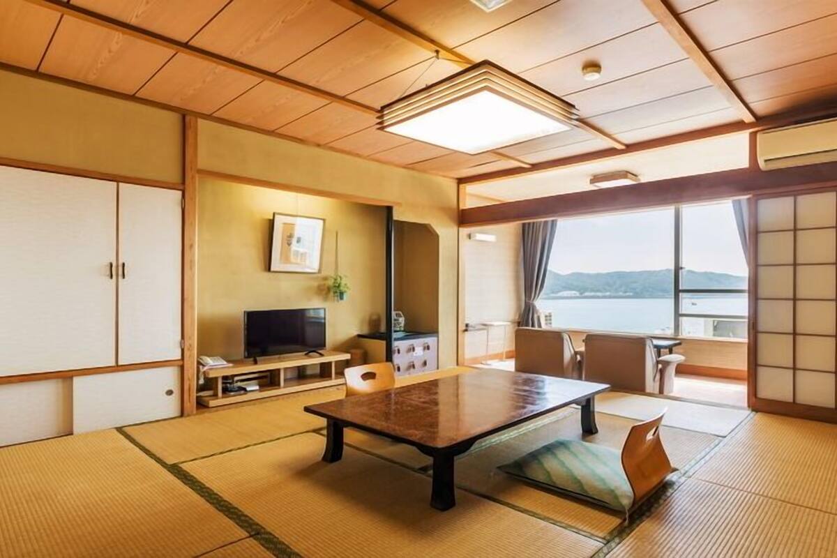 A traditional Japanese room with tatami flooring, a low table, a television, and a view of the water.