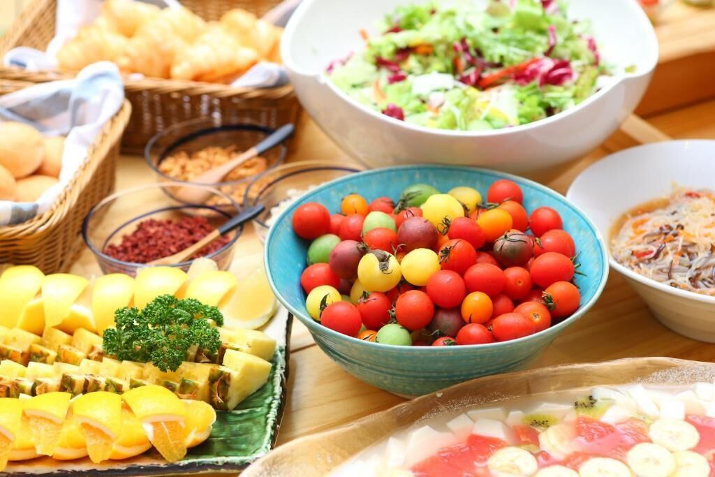 A table with various food items including a bowl of mixed cherry tomatoes, a bowl of salad, and other dishes.