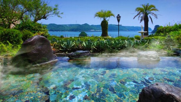 A clear pool with rocks and plants, surrounded by greenery and a view of the sea. - Kurofune Hotel (Shimoda)