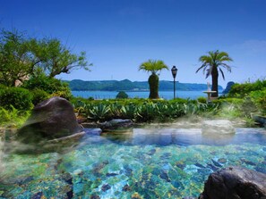 Ein klares Schwimmbecken mit Steinen und Pflanzen, umgeben von Grün und Blick aufs Meer.